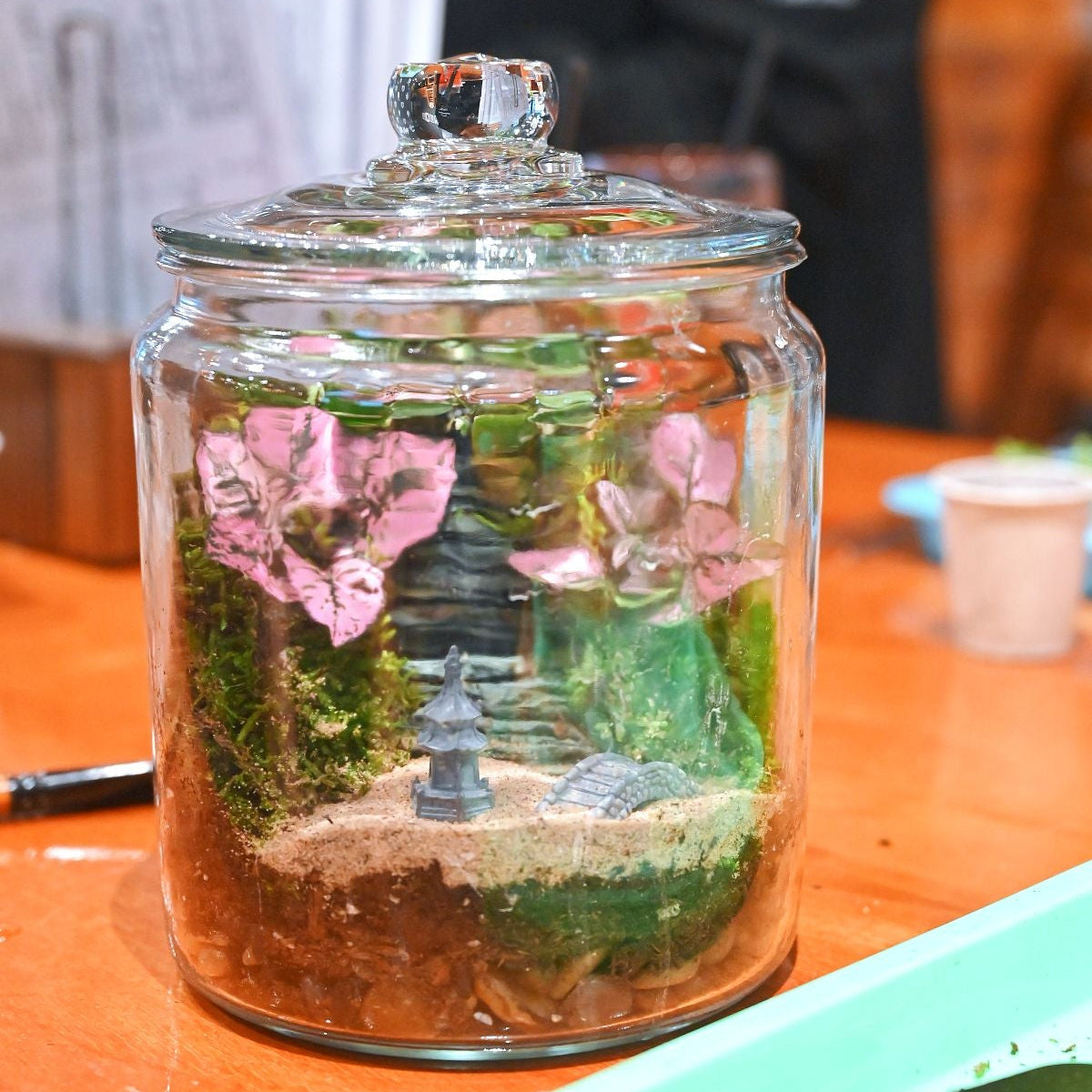 Decorative jar with plants and a small landscape on a table