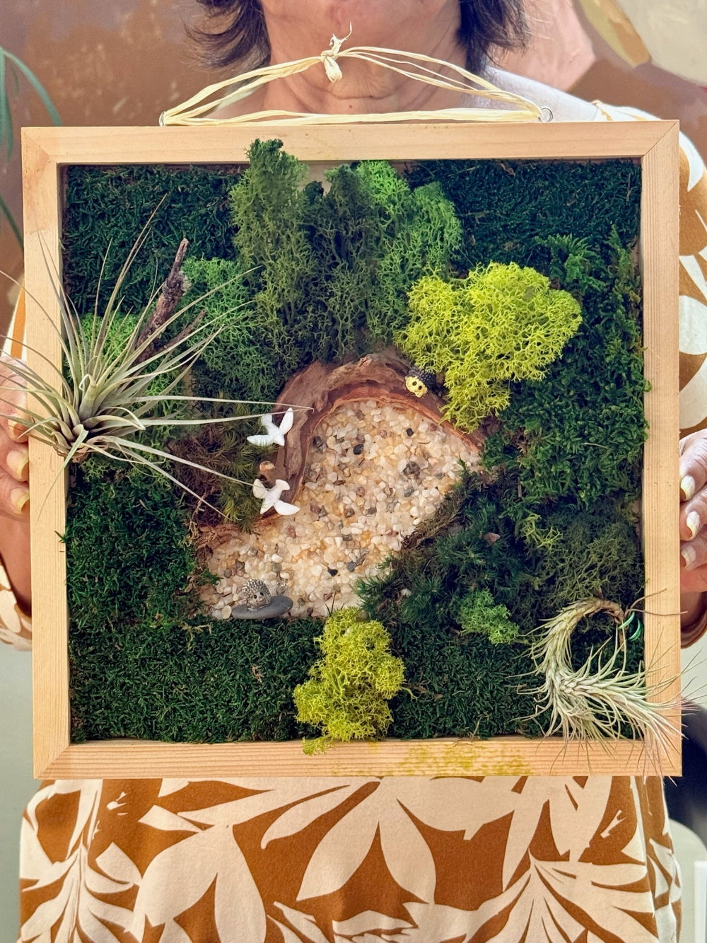 Moss wall art with plants and a wooden frame held by a person.