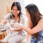 Two women sitting on a couch, one holding a terrarium, in a home setting.