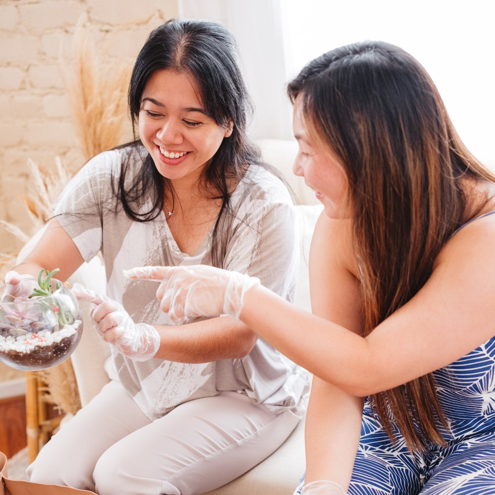 Two women sitting on a couch, one holding a terrarium, in a home setting.