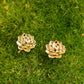 A pair of gold-toned flower stud earrings resting on a bed of green moss.