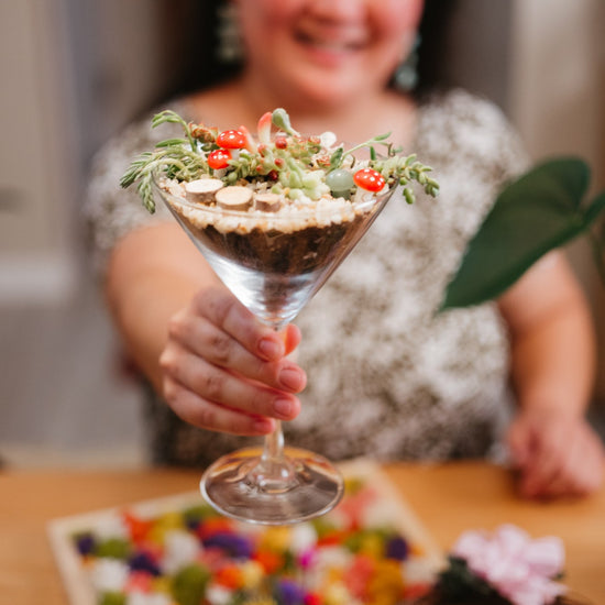 Person holding a glass with a plant decorative arrangement, blurred background