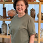 Woman wearing a green t-shirt with a plant design in front of a shelf with decorative items.