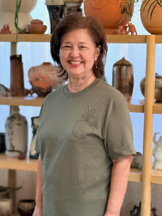 Woman wearing a green t-shirt with a plant design in front of a shelf with decorative items.