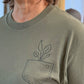Green sweatshirt with a plant design on the chest pocket worn by a person.