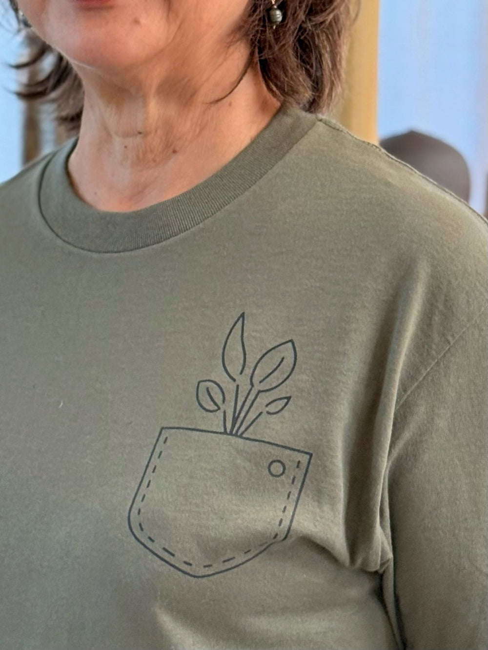 Green sweatshirt with a plant design on the chest pocket worn by a person.