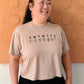 Person wearing a beige t-shirt with a printed design against an orange wall.