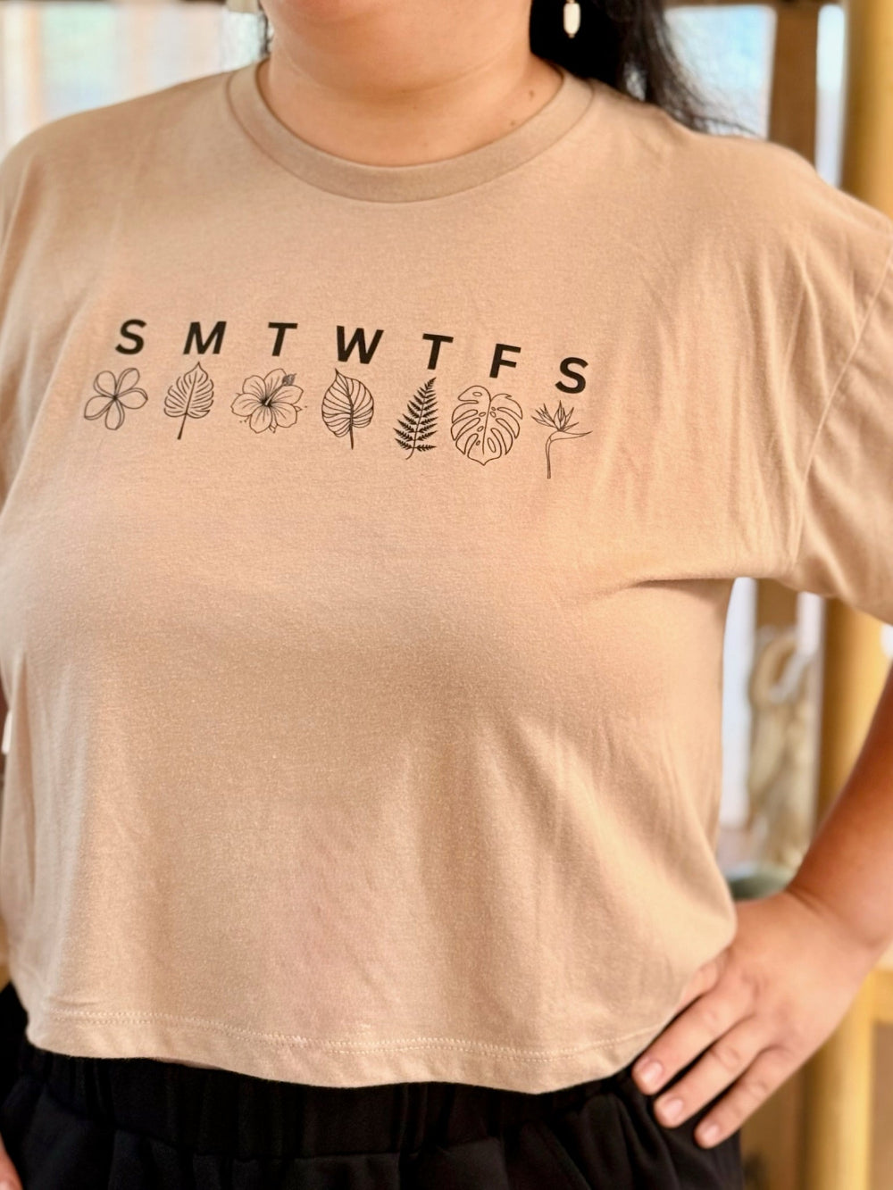 Beige t-shirt with 'SMTWTFSS' and leaf designs worn by a person.