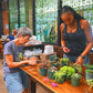 Two women working with plants at a table in a room with stained glass windows.