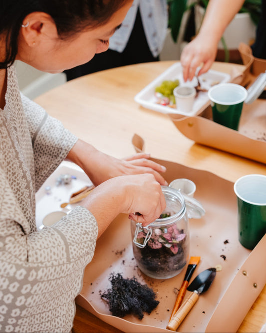 Person engaging in a gardening activity at a table with plants and tools.