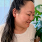 Woman with dark hair tied back, wearing a white top, indoors with blurred background
