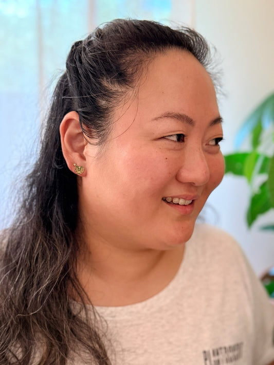 Woman with a ponytail wearing a white shirt with text, indoors with a blurred background