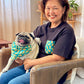 Woman sitting on a couch holding a pug wearing a colorful bandana in a cozy living room.