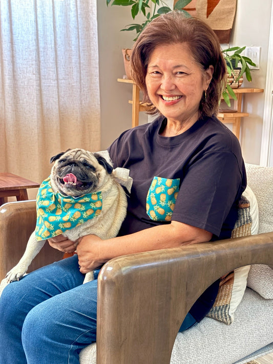 Woman sitting on a couch holding a pug wearing a colorful bandana in a cozy living room.