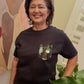 Woman wearing a black t-shirt with a graphic design, standing indoors against a colorful wall.