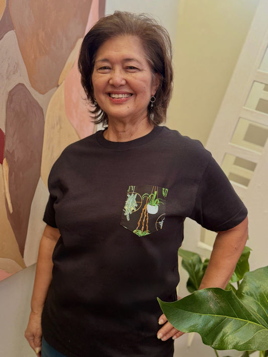 Woman wearing a black t-shirt with a graphic design, standing indoors against a colorful wall.